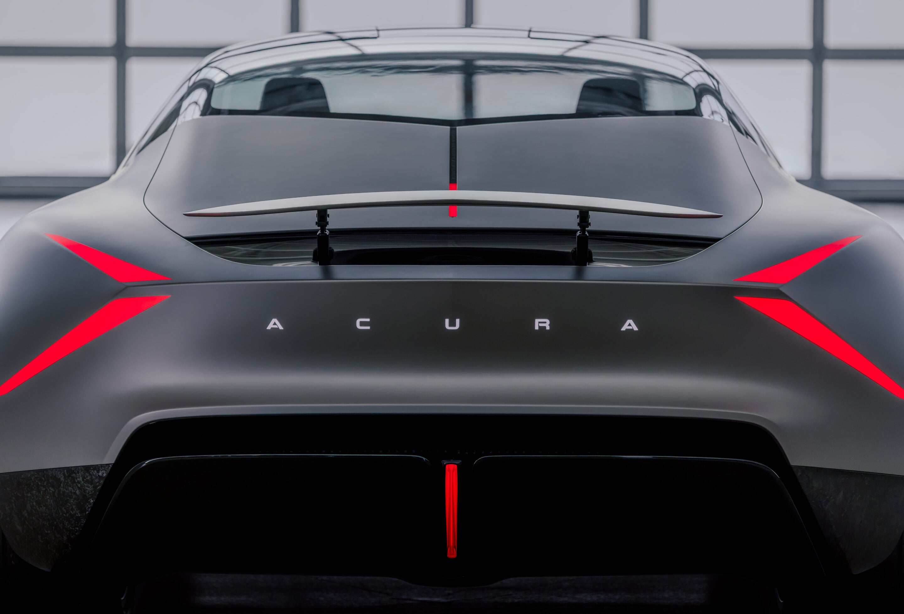 Rear view of a dark, high-performance car with a central red accent line and spoiler highlights.