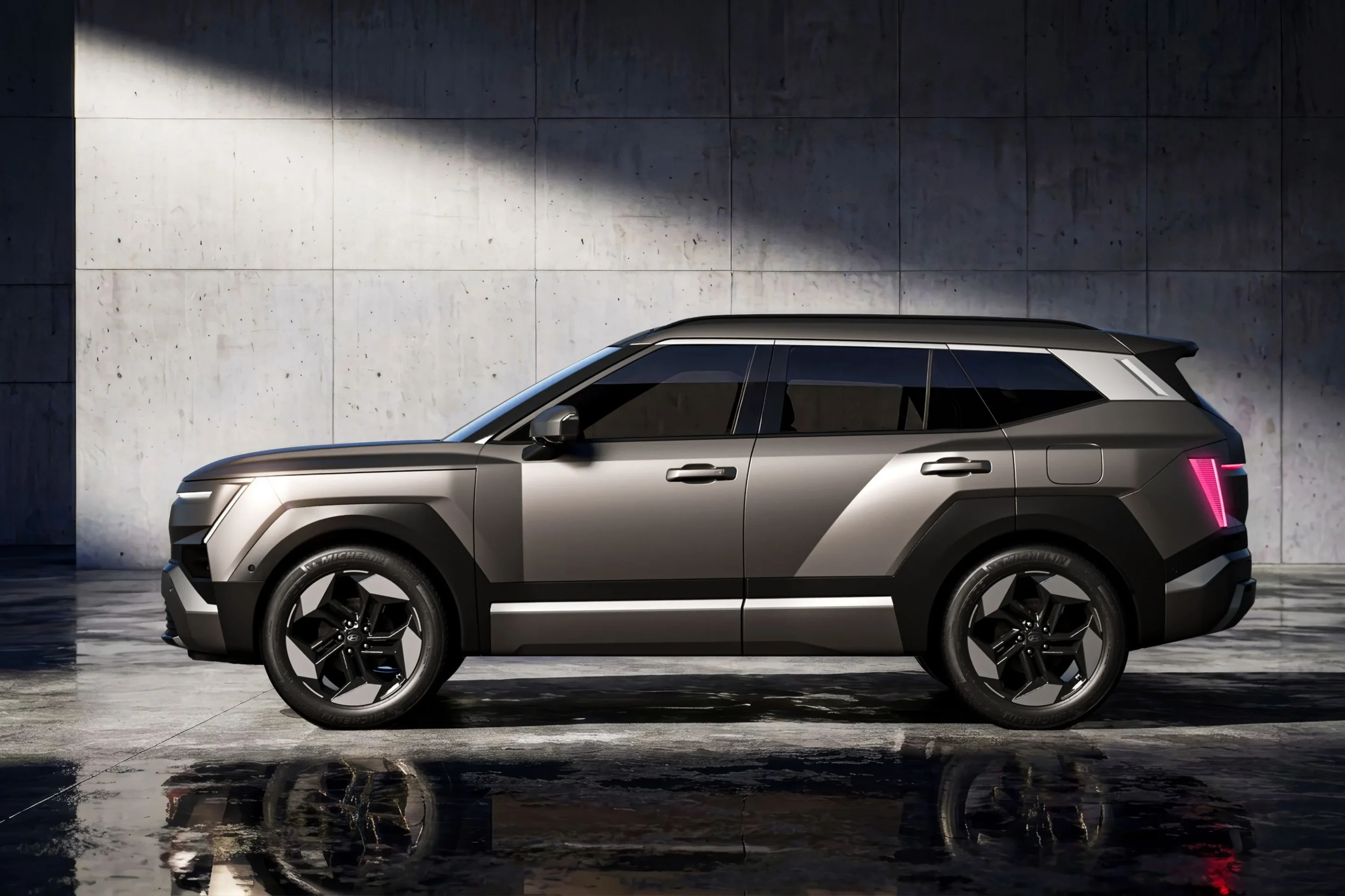 Side view of a silver-gray SUV with black trim parked indoors against a textured concrete wall, reflecting on a wet floor.