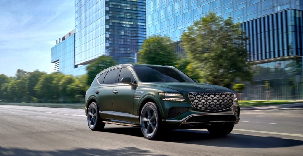 Green luxury SUV driving on a city street with glass office buildings in the background
