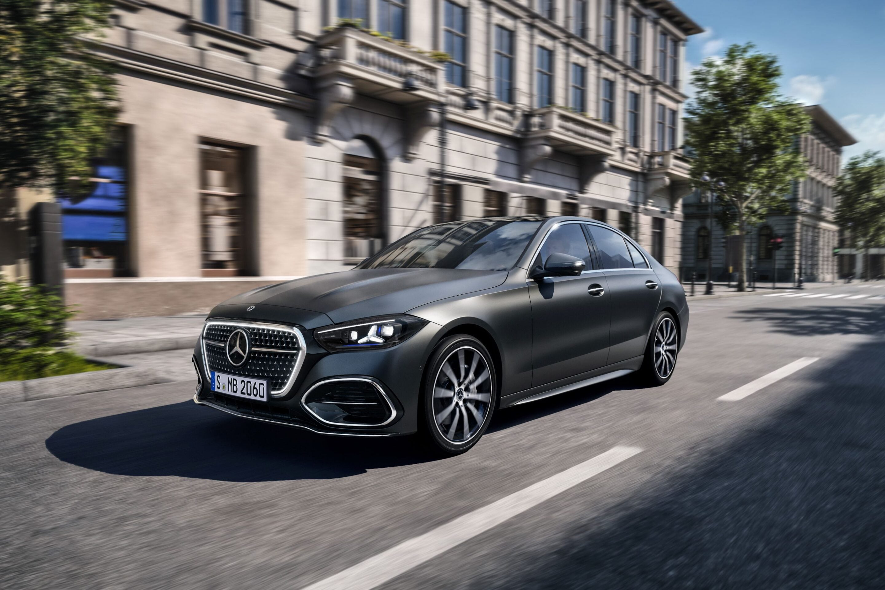 Gray Mercedes-Benz sedan driving on a city street, buildings blurred in the background from motion.
