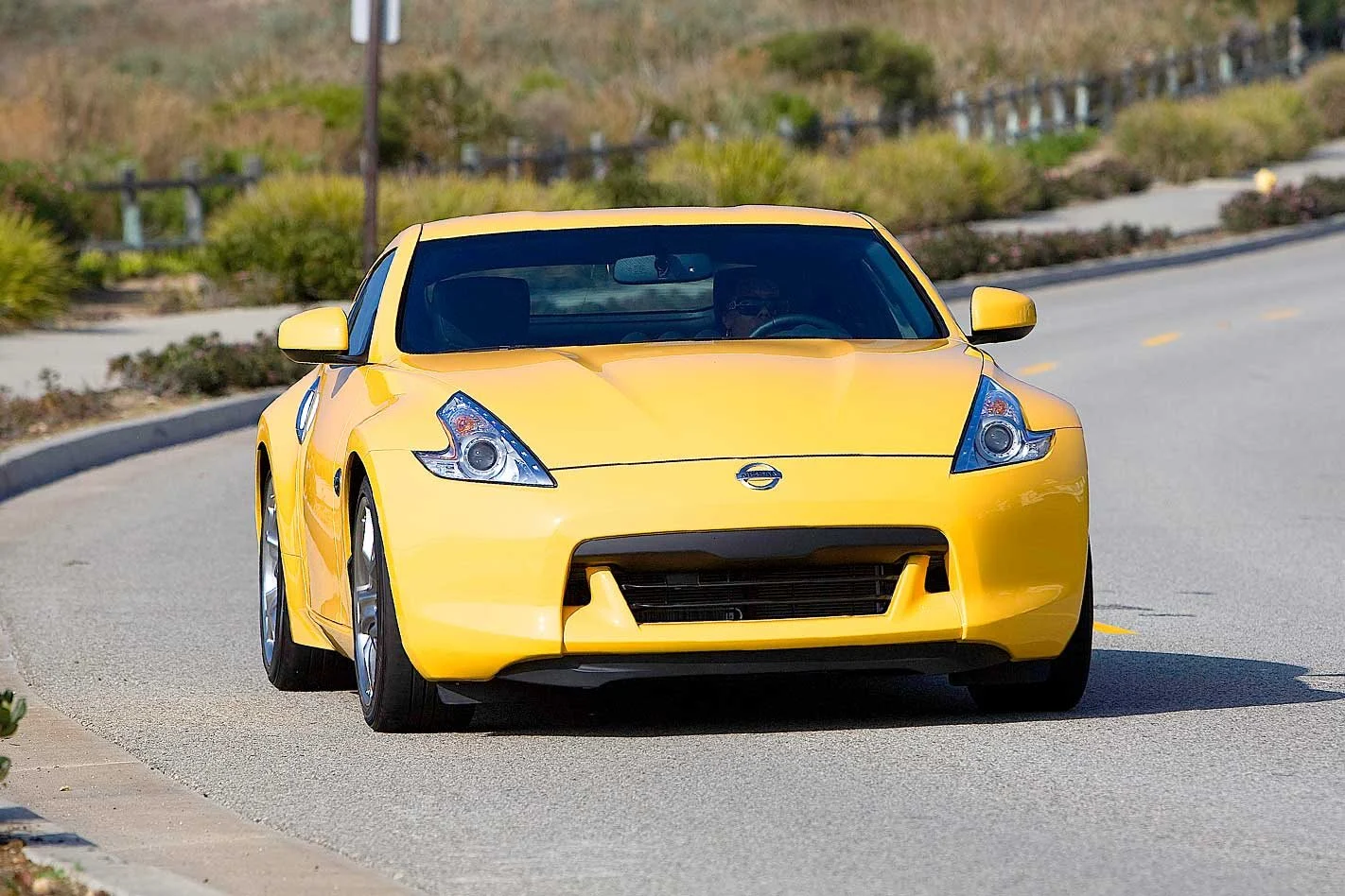Front view of a bright yellow Nissan sports car driving on a curved suburban road
