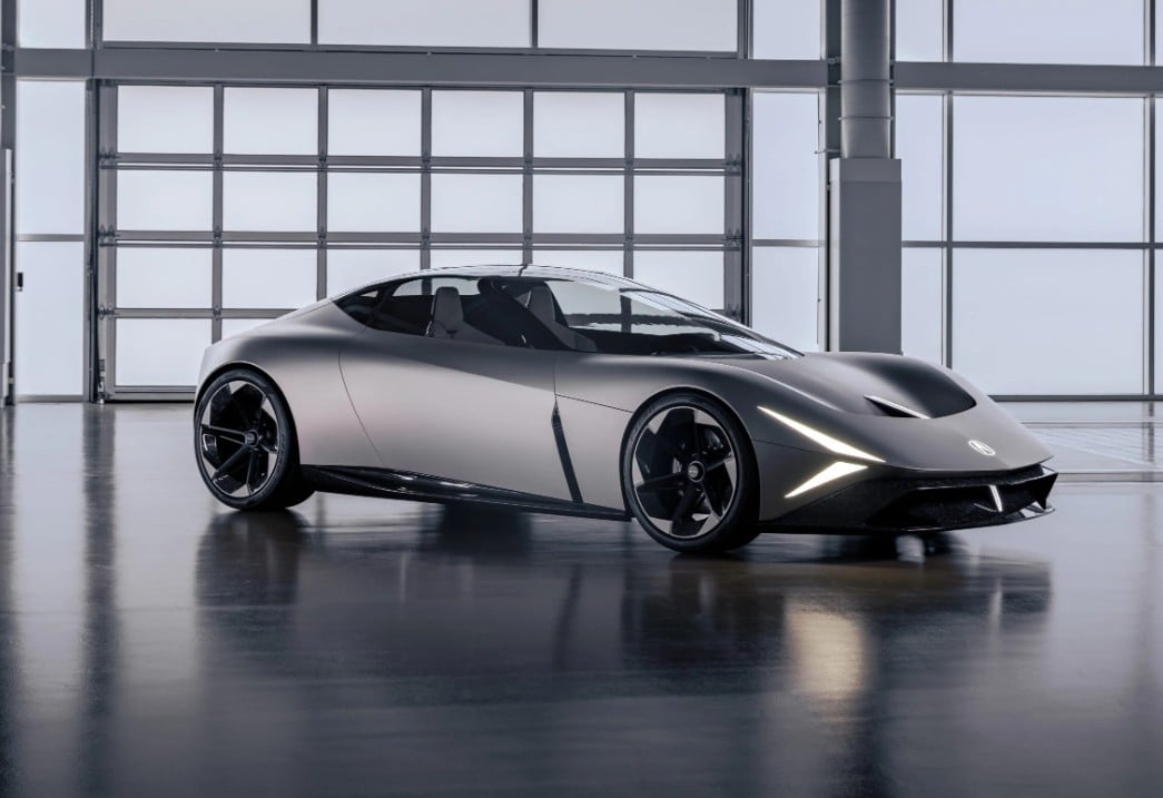 Silver futuristic sports car in a modern showroom with large glass walls and bright lighting, headlights on.