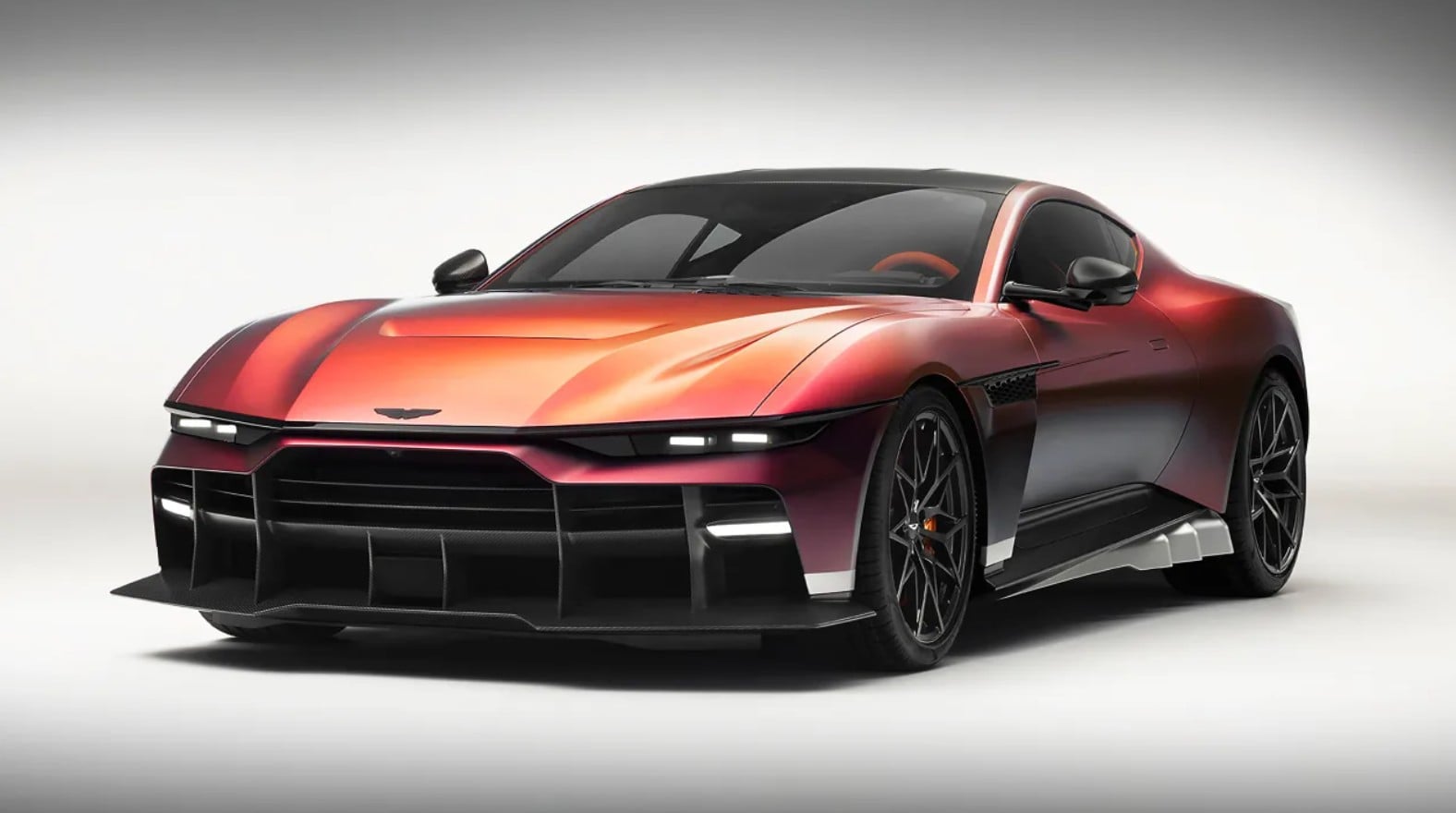 Red low-profile sports car with a black roof, prominent front splitter, and large dark wheels in a studio setting.