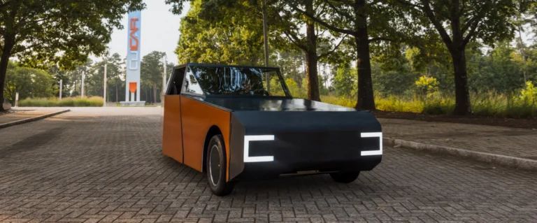 Futuristic black-and-wood panel car parked on a brick street with a tall orange-and-blue sign in the background.