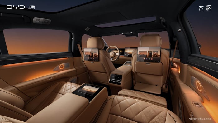 Luxurious tan leather SUV interior with rear-seat entertainment screens and ambient lighting at dusk/amber glow, spacious and upscale setting.