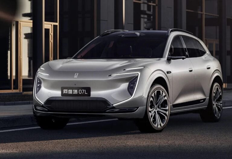 Front three-quarter view of a silver electric SUV with sleek LED headlights parked on a city street at night.
