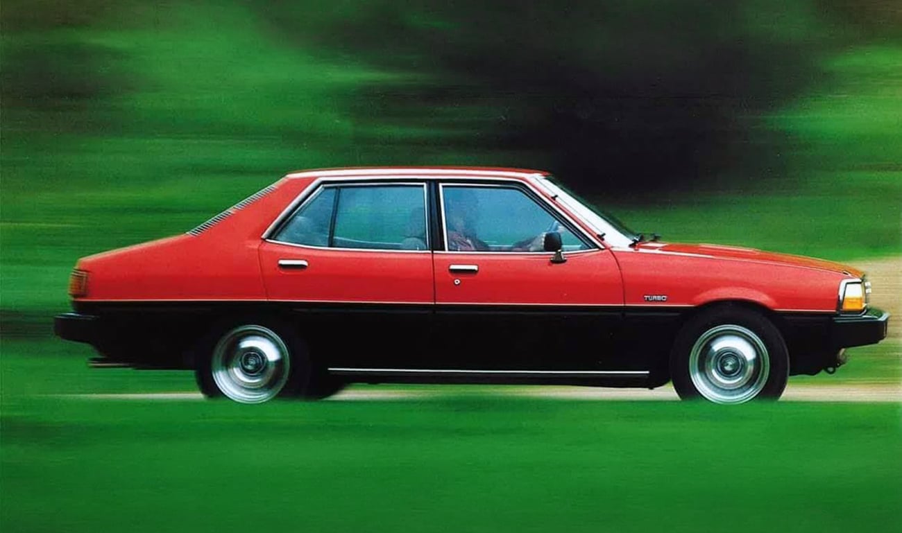 Red four-door sedan in motion, driving on a green blurred background (vintage car with black bumper).
