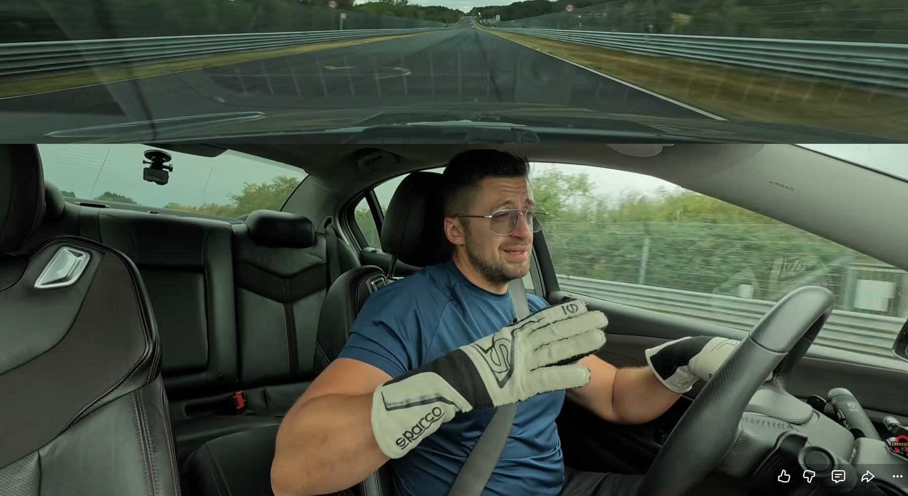 Man driving a car on a highway, wearing a seatbelt and racing-style gloves; road ahead visible through windshield.
