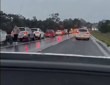 Line of cars stuck in heavy traffic on a wet highway, rain-soaked road and reflections visible, photo taken from inside a car window.