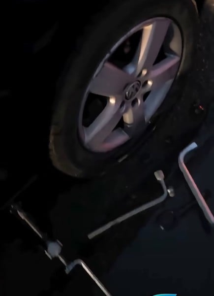 Toyota alloy wheel on the ground with a tire, nearby scattered lug wrench and repair tools.