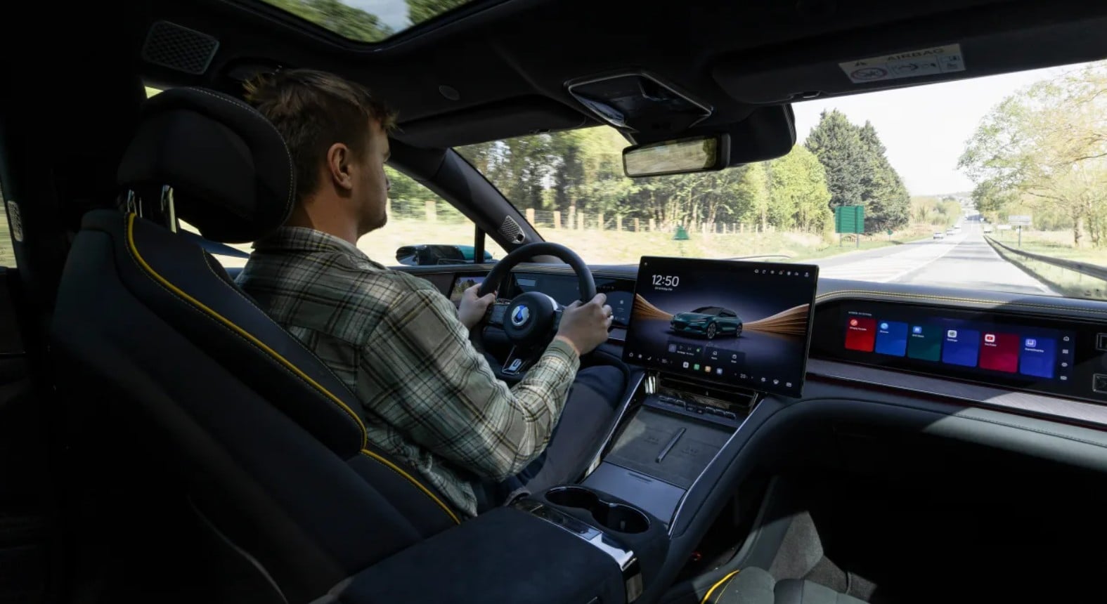 Driver seated in a modern car interior with a large touchscreen infotainment display and digital dashboard as they drive on a highway