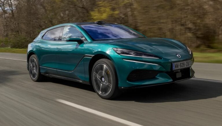 Teal BMW sports coupe speeding along a rural road with trees in the background.