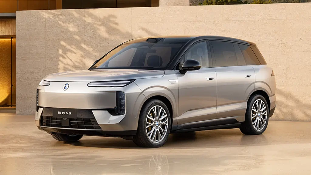 Three-quarter front view of a silver electric SUV parked outdoors against a beige wall.