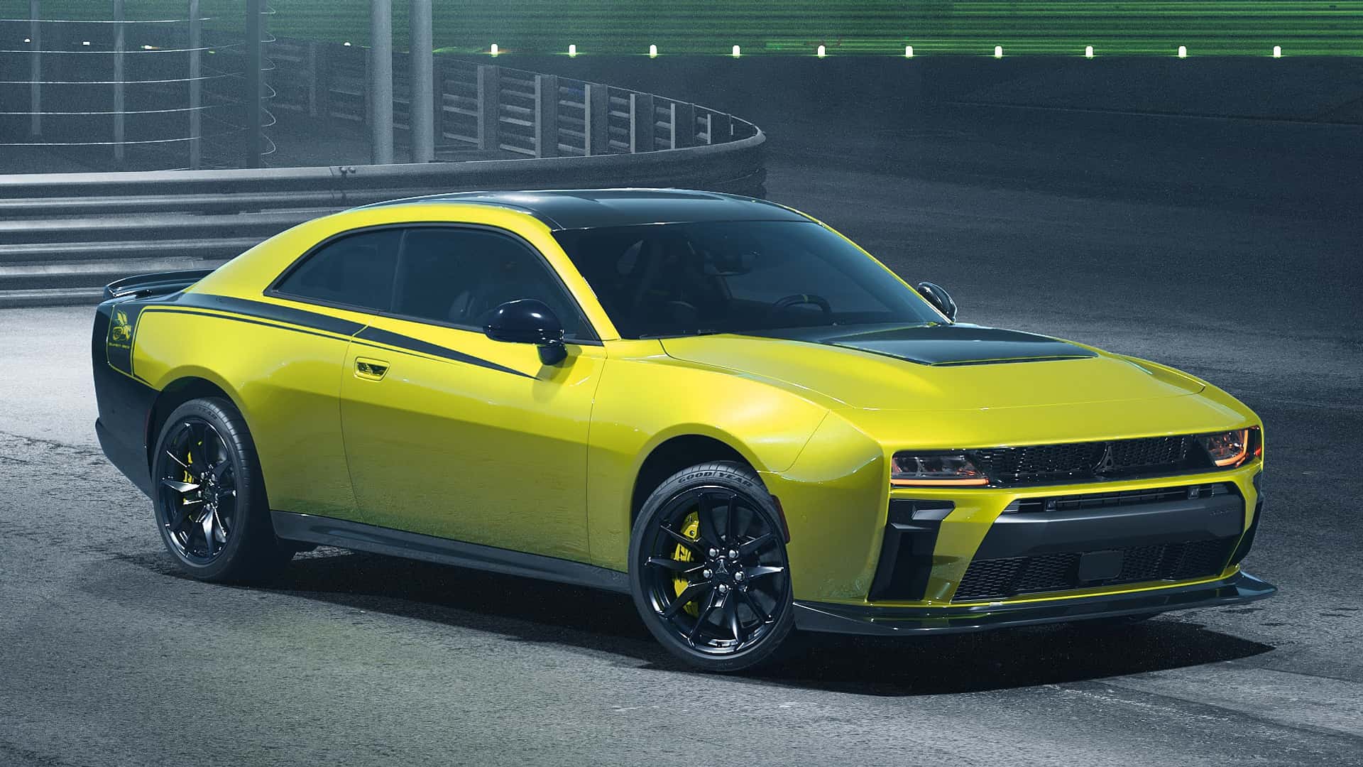 Yellow sports car with black hood and roof parked on a racing track, front three-quarter view with black wheels and accent stripes