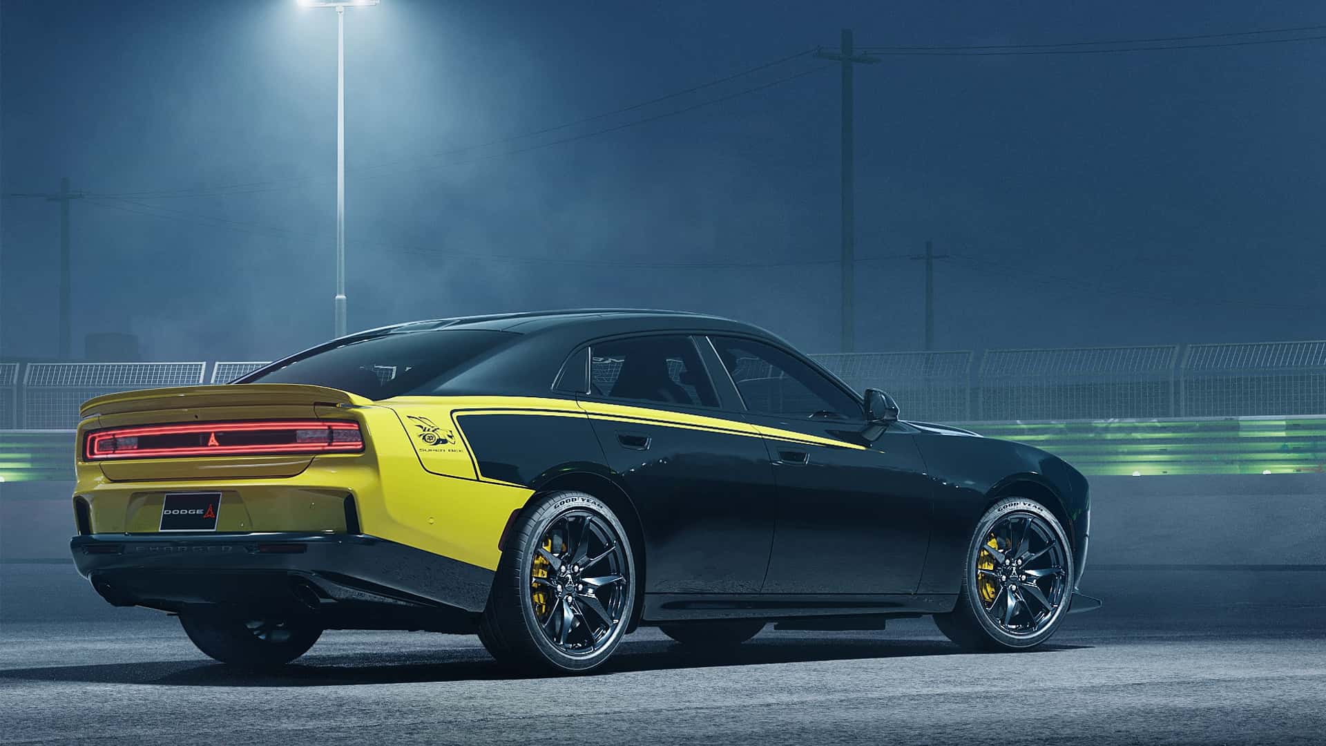 Rear and side view of a yellow and black Dodge sports coupe on a race track at night under stadium lights to emphasize speed and racing.