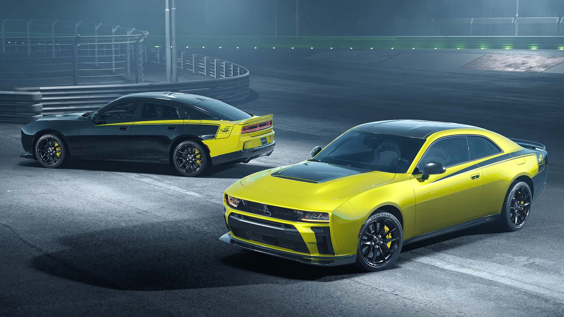 Two high‑performance cars in yellow and black sit on a dark race track at night, with safety barriers and green lights in the background.