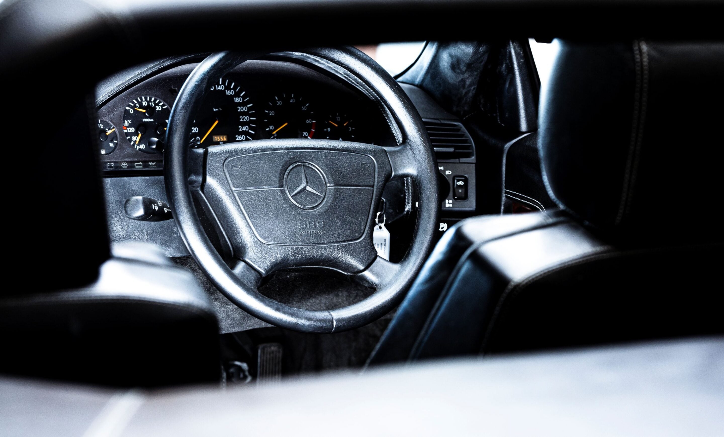Close-up of a Mercedes steering wheel with the instrument cluster visible in the dim dashboard background