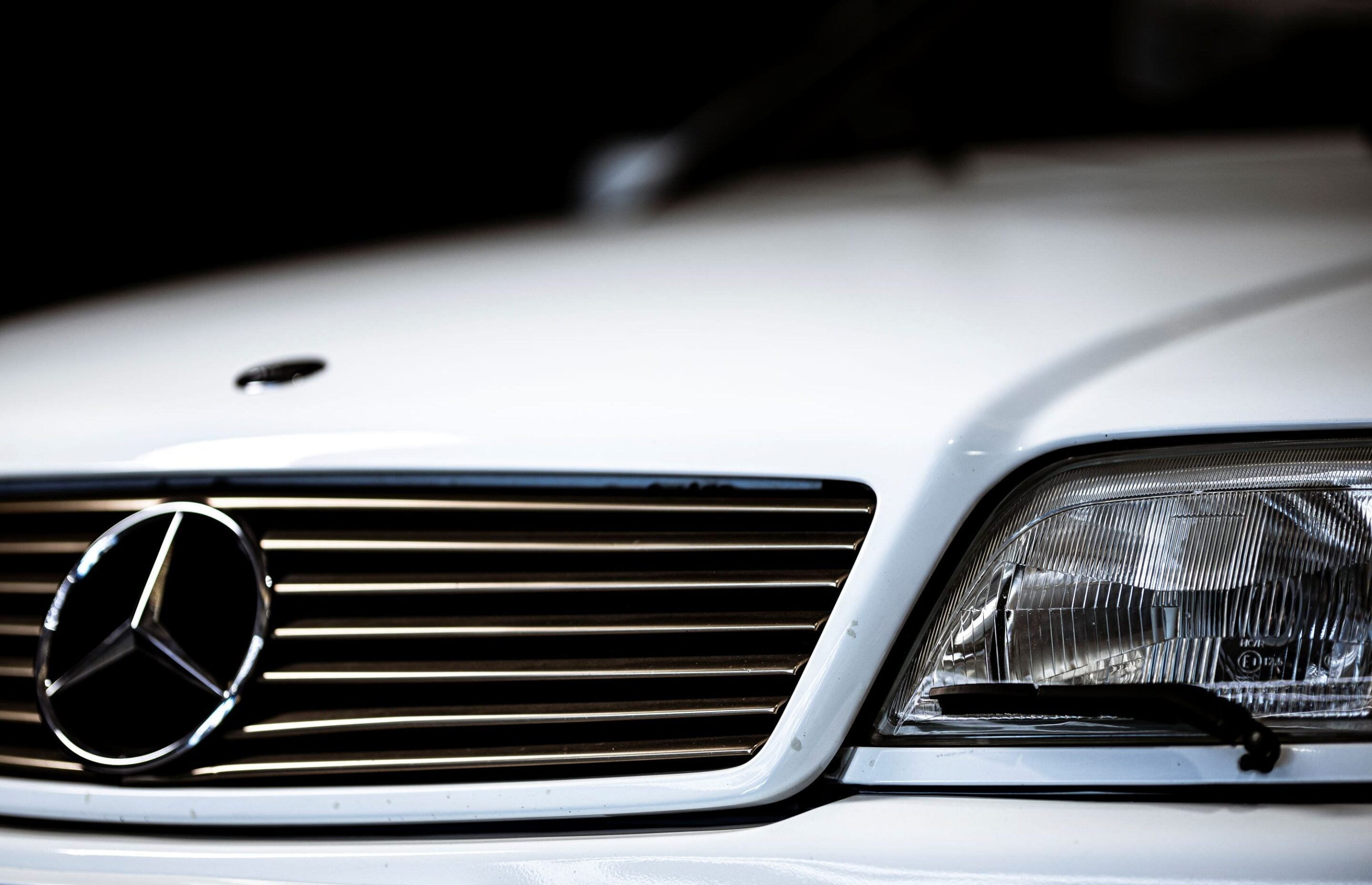 Close-up of a white Mercedes-Benz front grille with emblem and a headlight to the right.