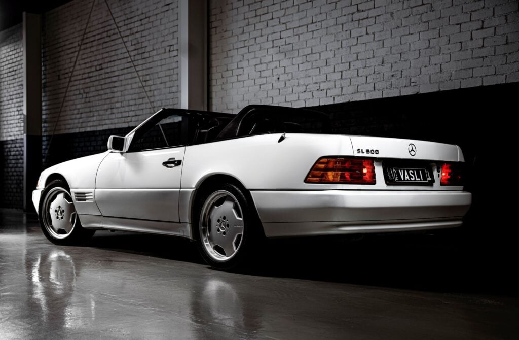 White Mercedes-Benz SL500 convertible parked in a dim garage with brick walls in the background, rear quarter view.