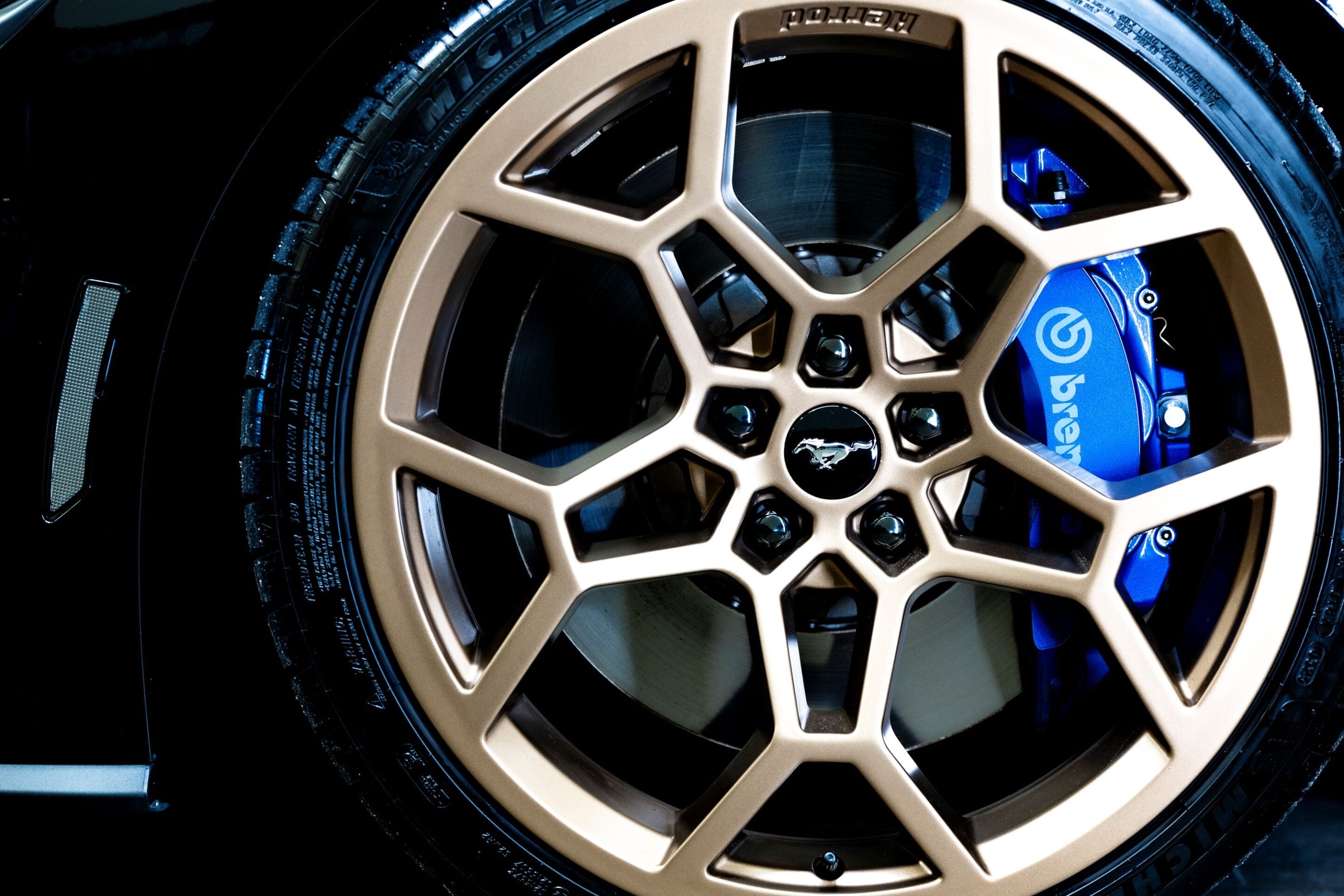 Close-up of a gold multi-spoke alloy wheel with a blue Brembo brake caliper and Mustang emblem at the center cap.