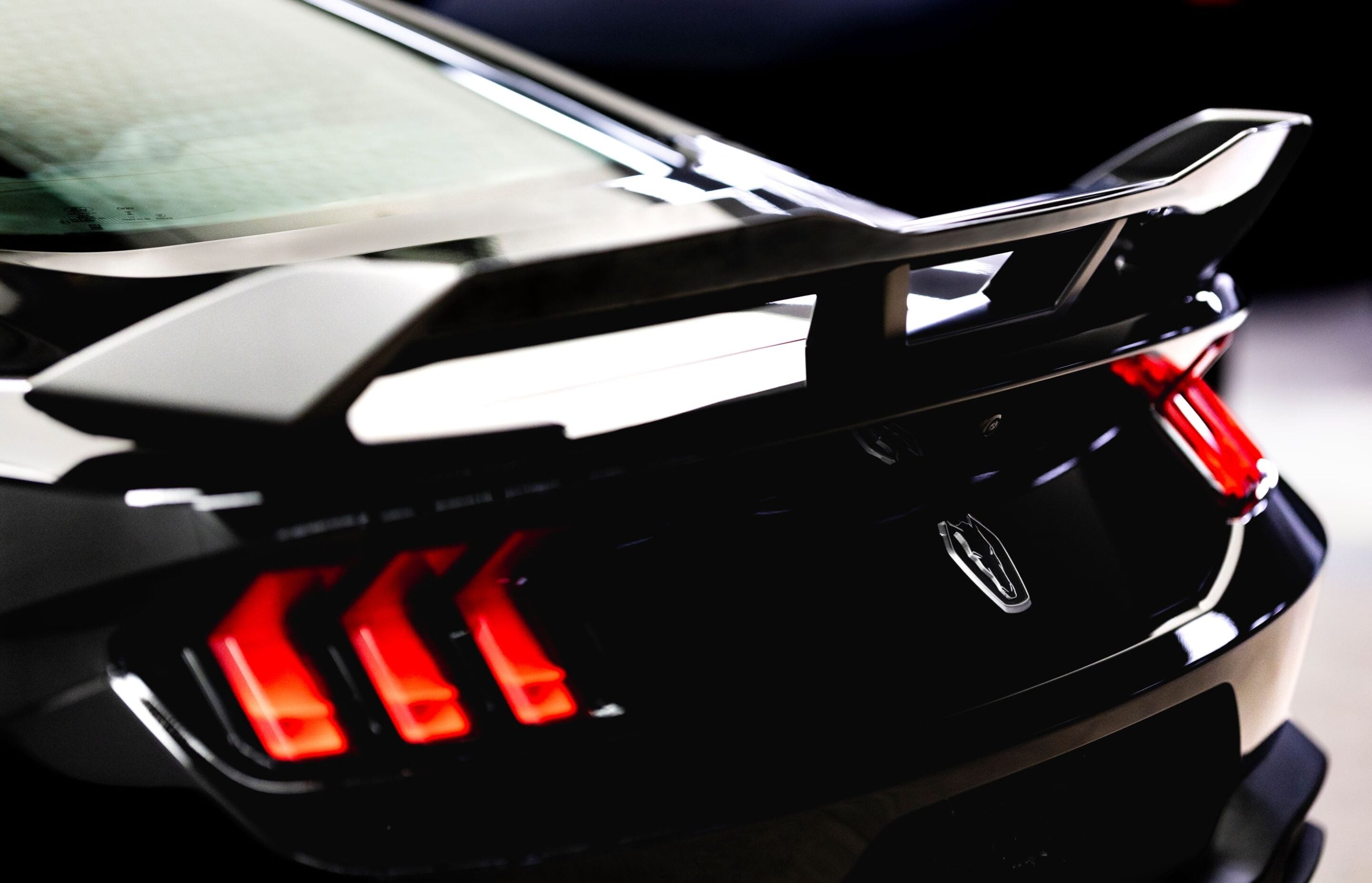 Close-up of the rear end of a black car showing red taillights and a chrome badge on the trunk rim.