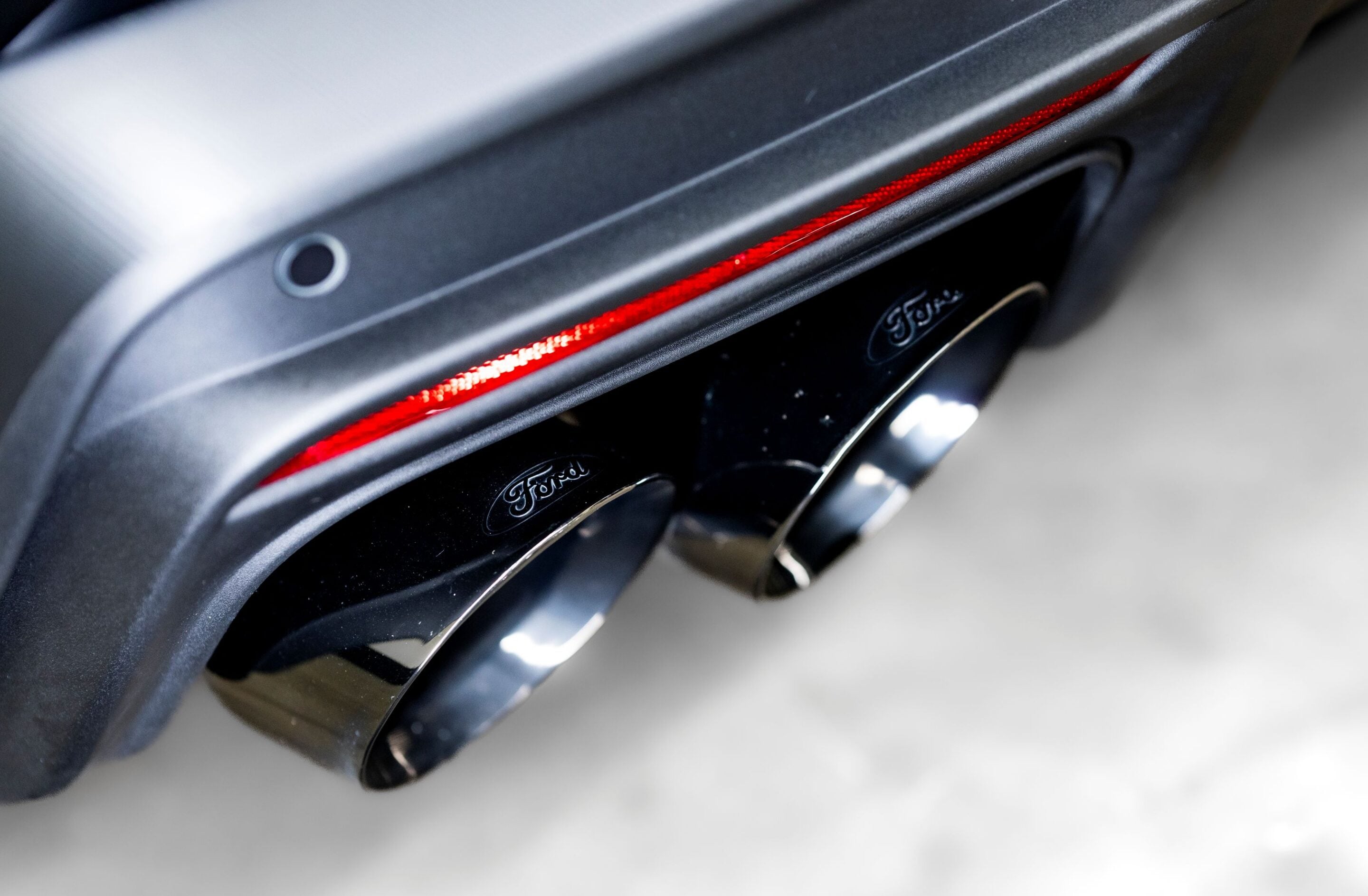Close-up of a Ford badge on a car's rear, with a red taillight stripe along the edge
