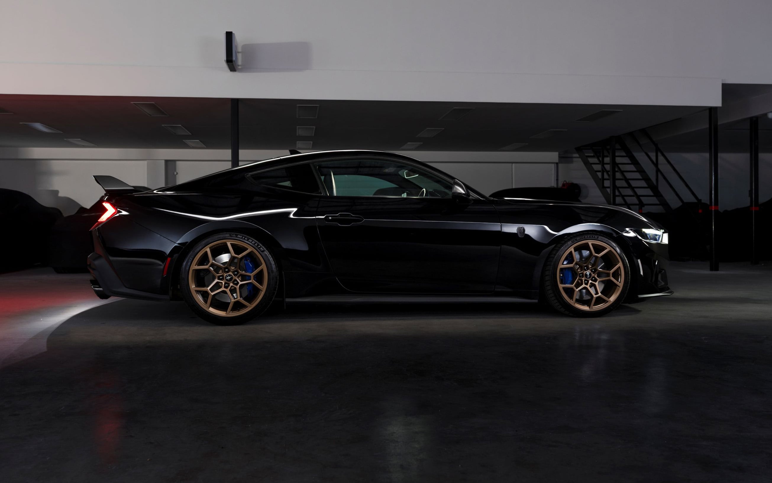Black sports car with bronze wheels parked in a dim showroom interior.