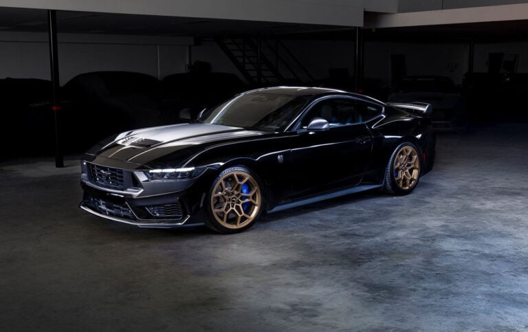 Front three-quarter view of a glossy black Ford Mustang with bronze/gold wheels in a dim showroom light.