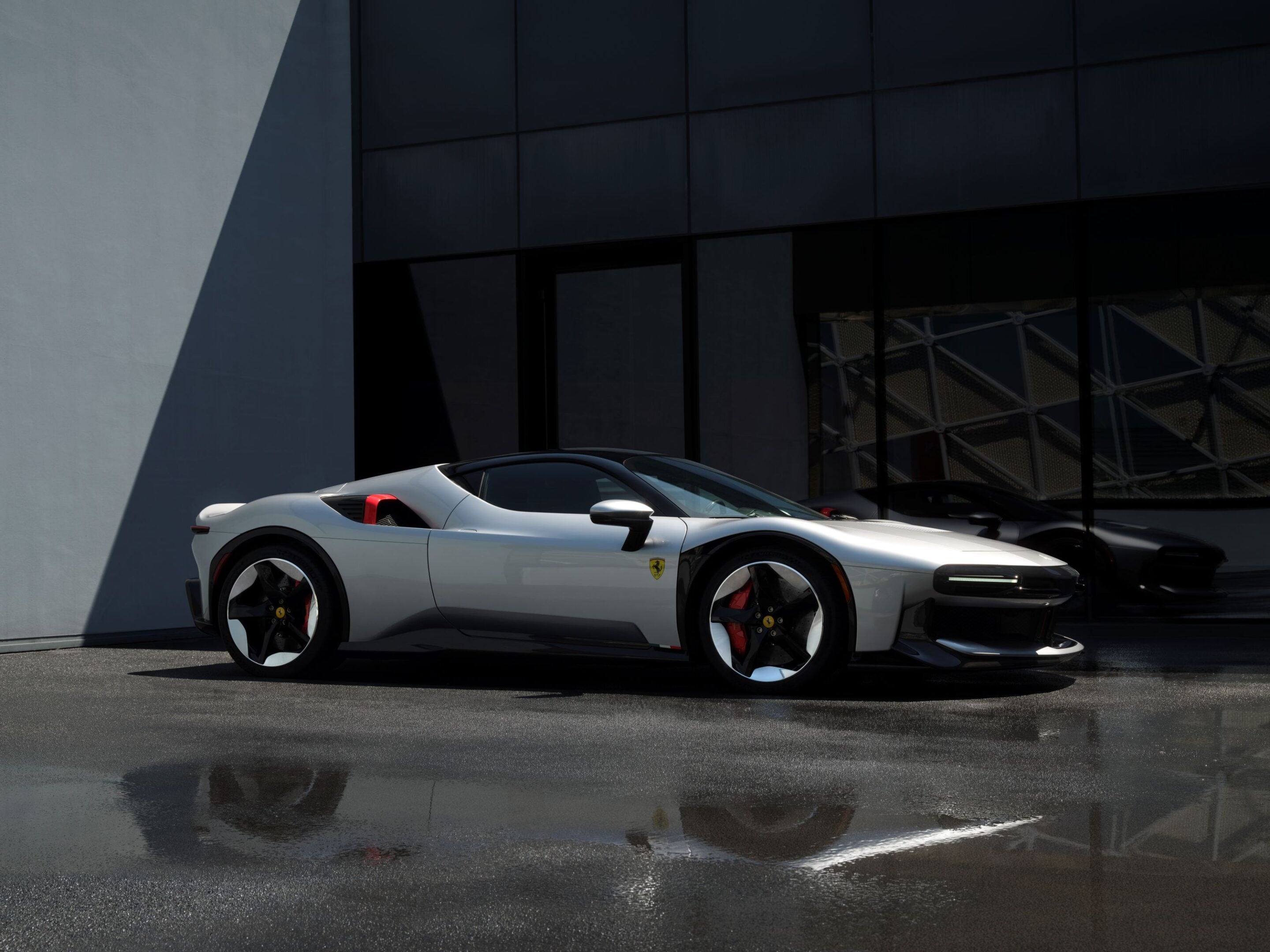 Two silver Ferrari sports cars parked side by side in front of a modern glass-front building.