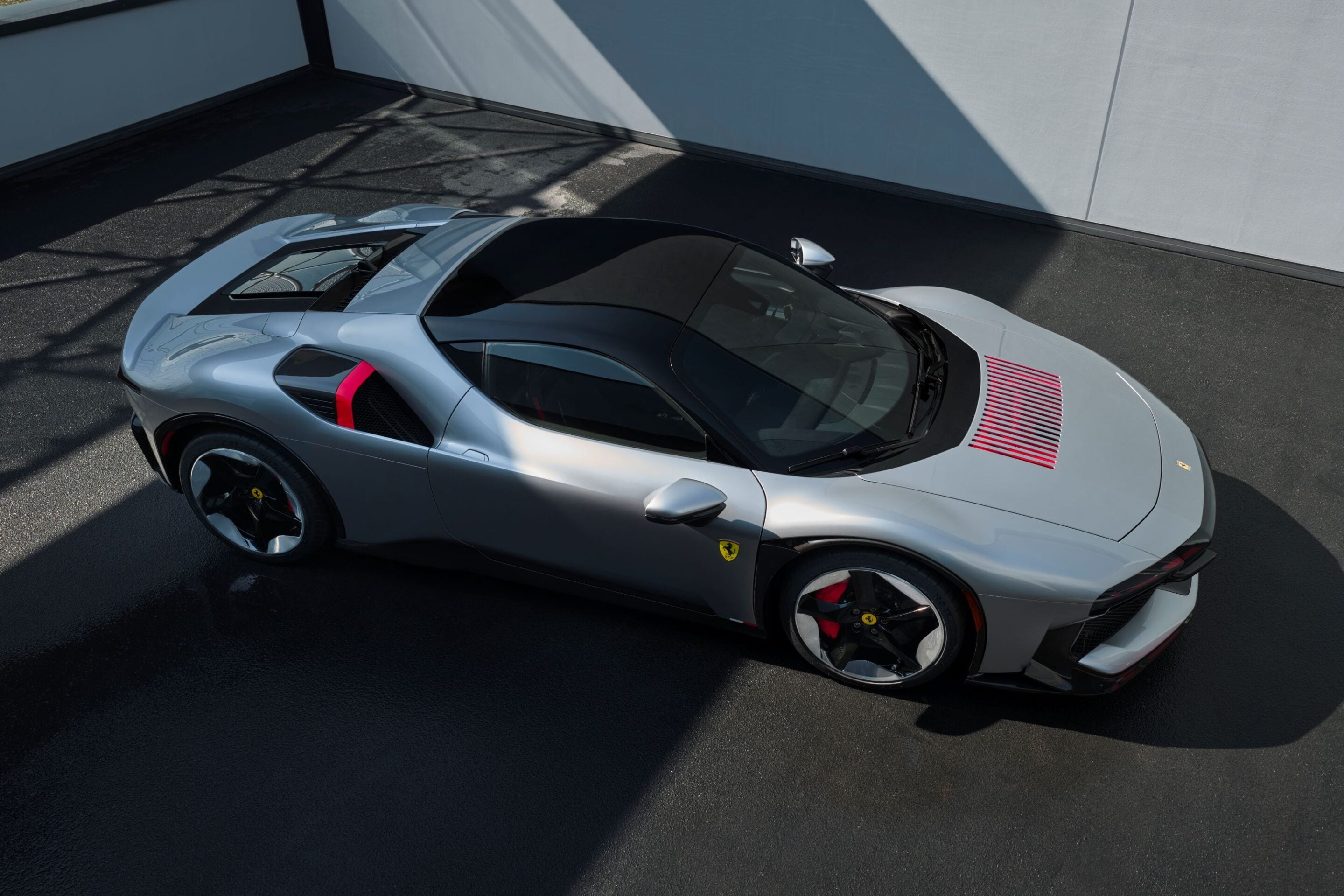 Top-down shot of a silver Ferrari sports car with red accents parked on dark asphalt.