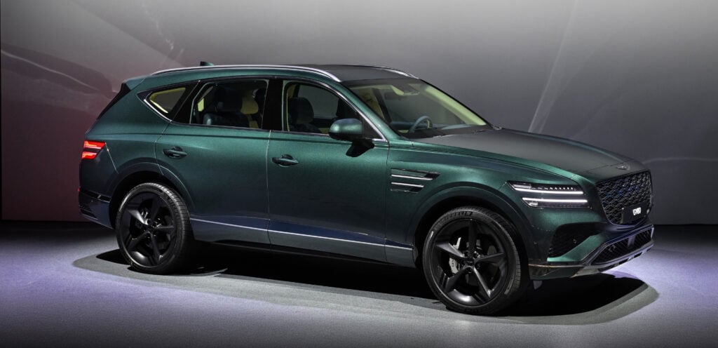 Green Genesis GV80 SUV on a showroom floor, angled side view with sunroof visible.