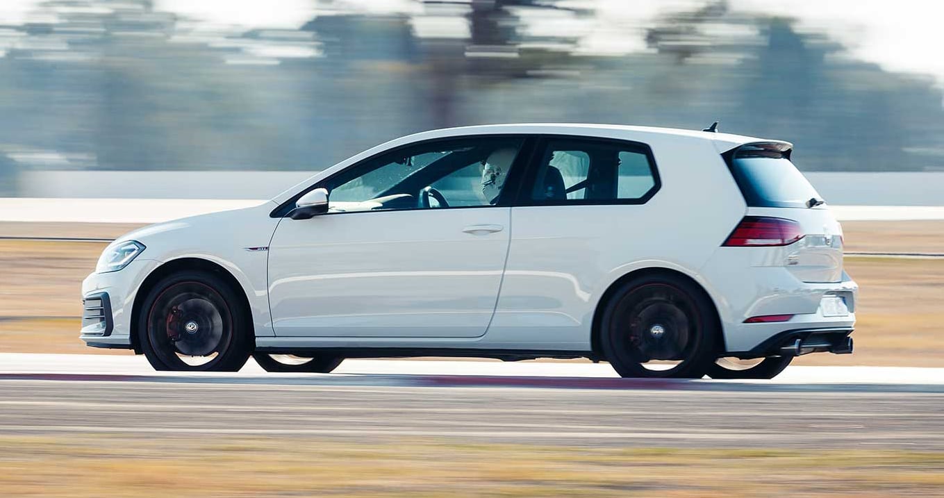 White hatchback car speeding on a race track with motion blur in the background, side view