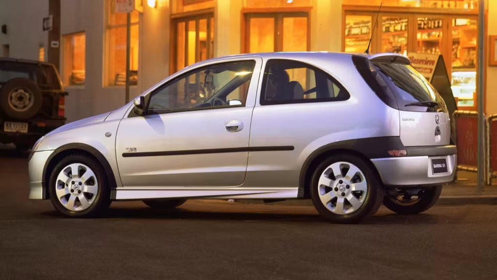 Silver hatchback parked on a city street at dusk with warmly lit shop windows in the background.