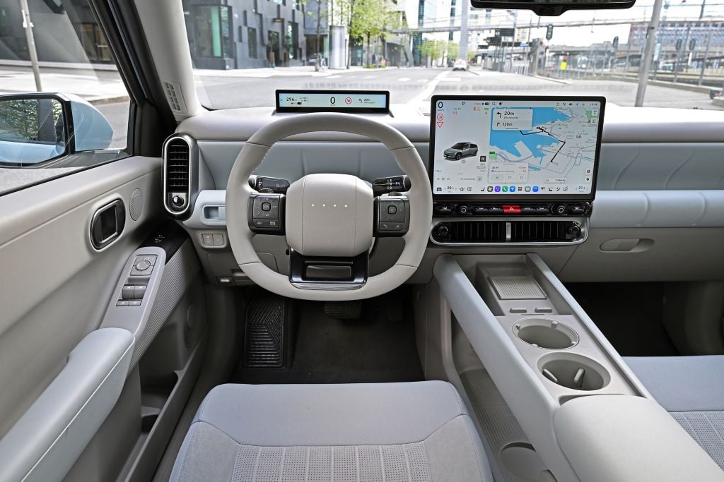 Front interior of a modern car with a round steering wheel and a wide touchscreen map display on the dash.
