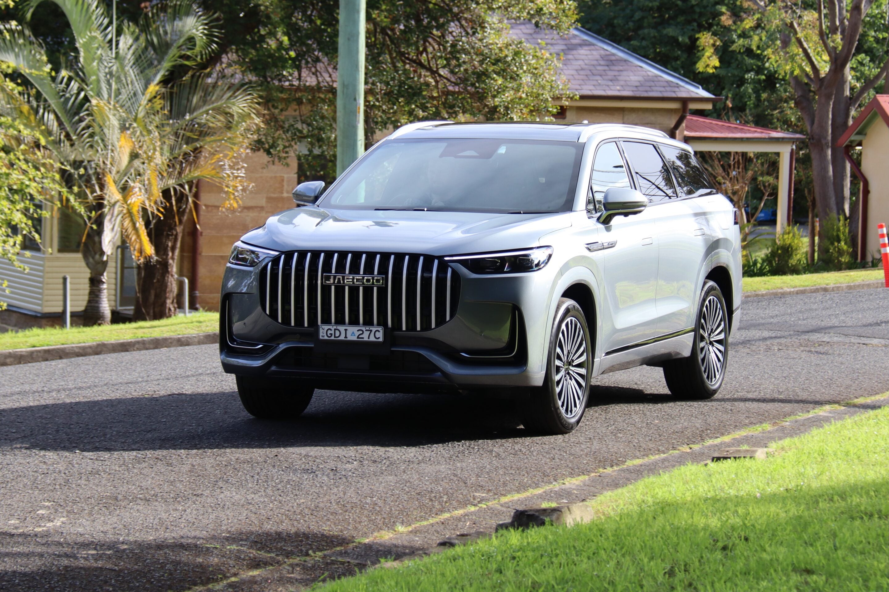 Silver SUV parked on a residential street, front grille and headlights visible with green lawn and houses in the background