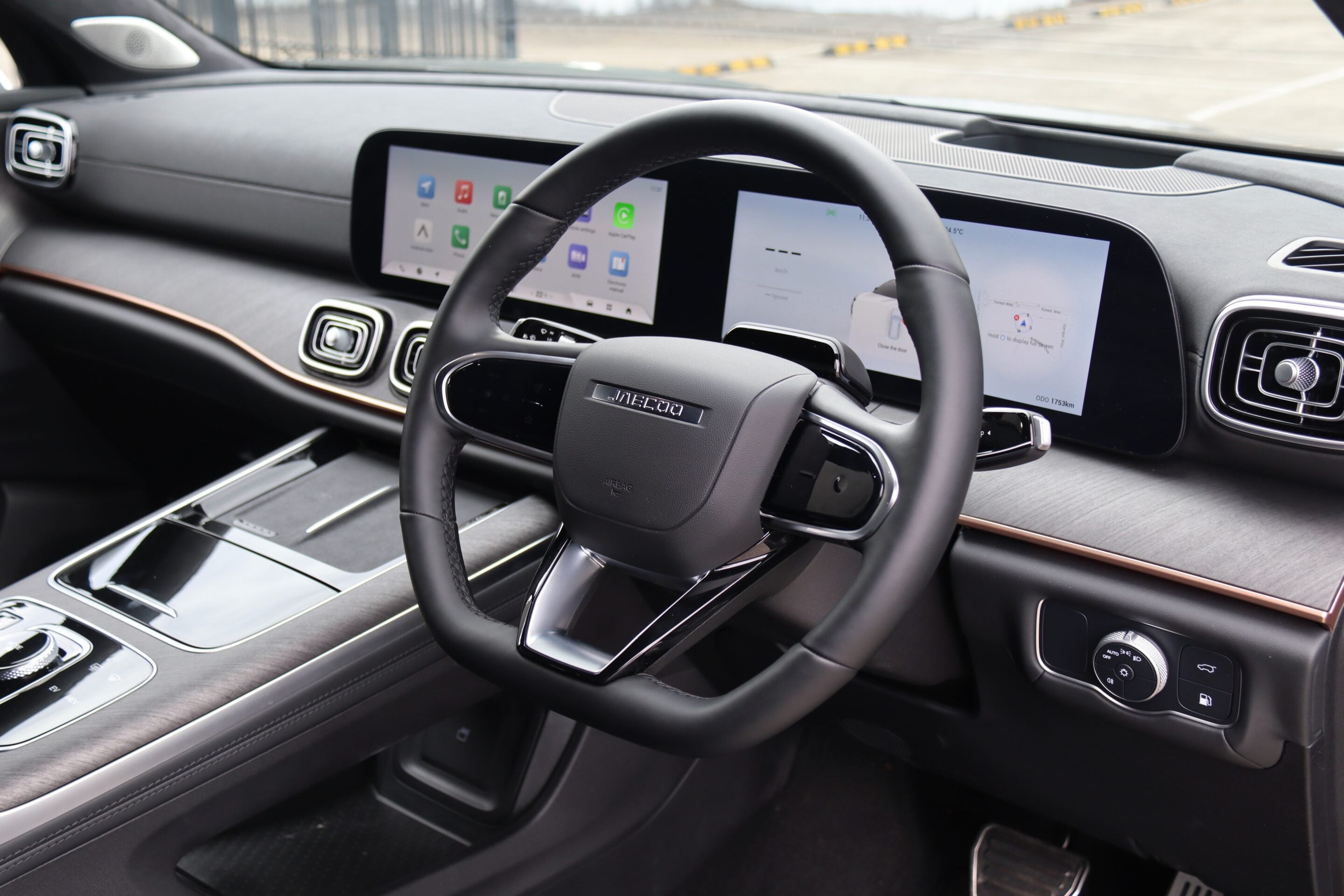 Steering wheel centered in a car interior with two wide digital screens on the dashboard and glossy controls along the center console.