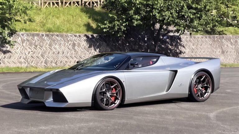 Silver mid‑engine sports car with black roof, red brake calipers, and large rear wing parked on pavement