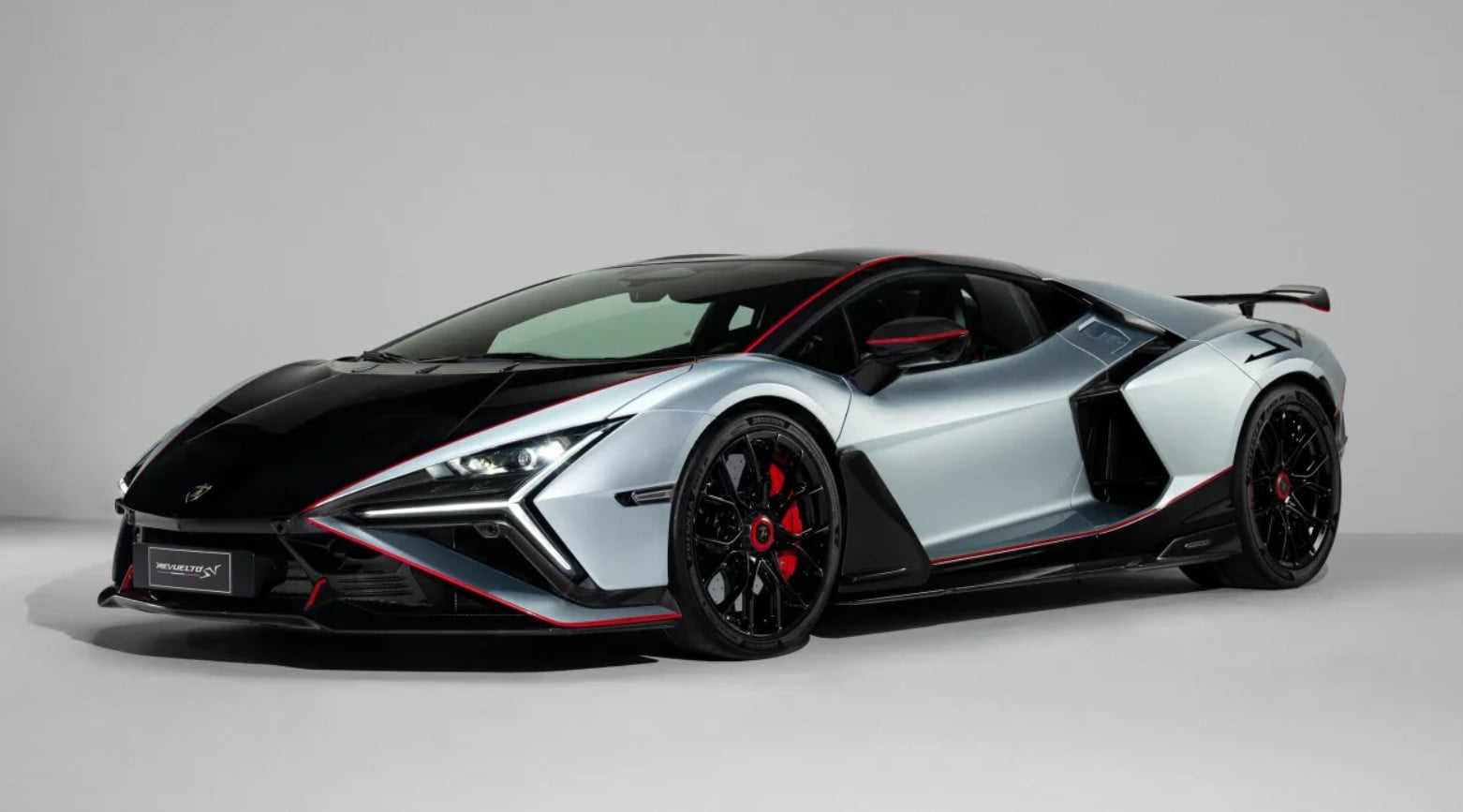 Front three-quarter view of a silver-and-black Lamborghini hypercar with red accents in a studio setting, low and aggressive stance.
