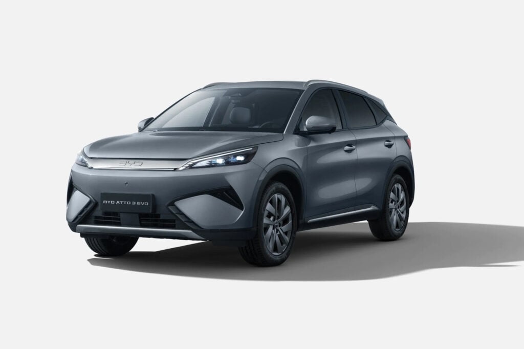 Three-quarter front view of a silver BYD Atto 3 EV SUV on a light background, showing its grille and LED headlights.