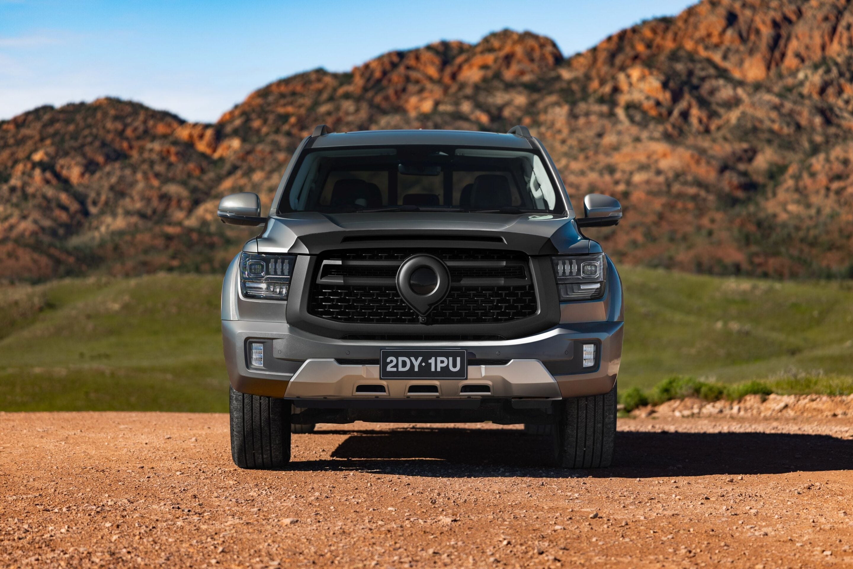 Front view of a silver pickup truck parked on a dirt road with rocky hills in the background, license plate reading 2DY 1PU forground center.