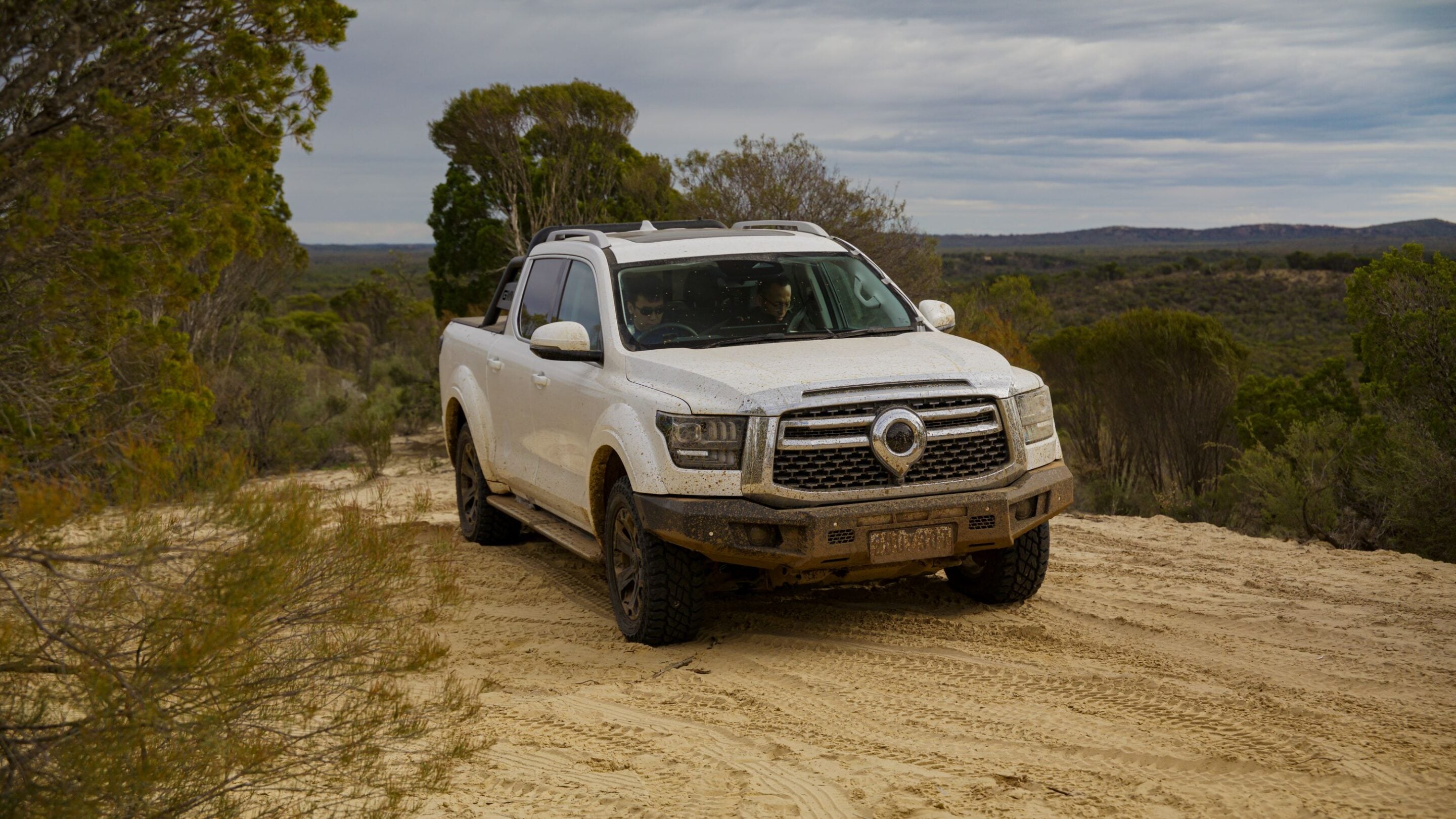 White pickup truck driving off-road on a sandy desert trail, muddy and rugged.
