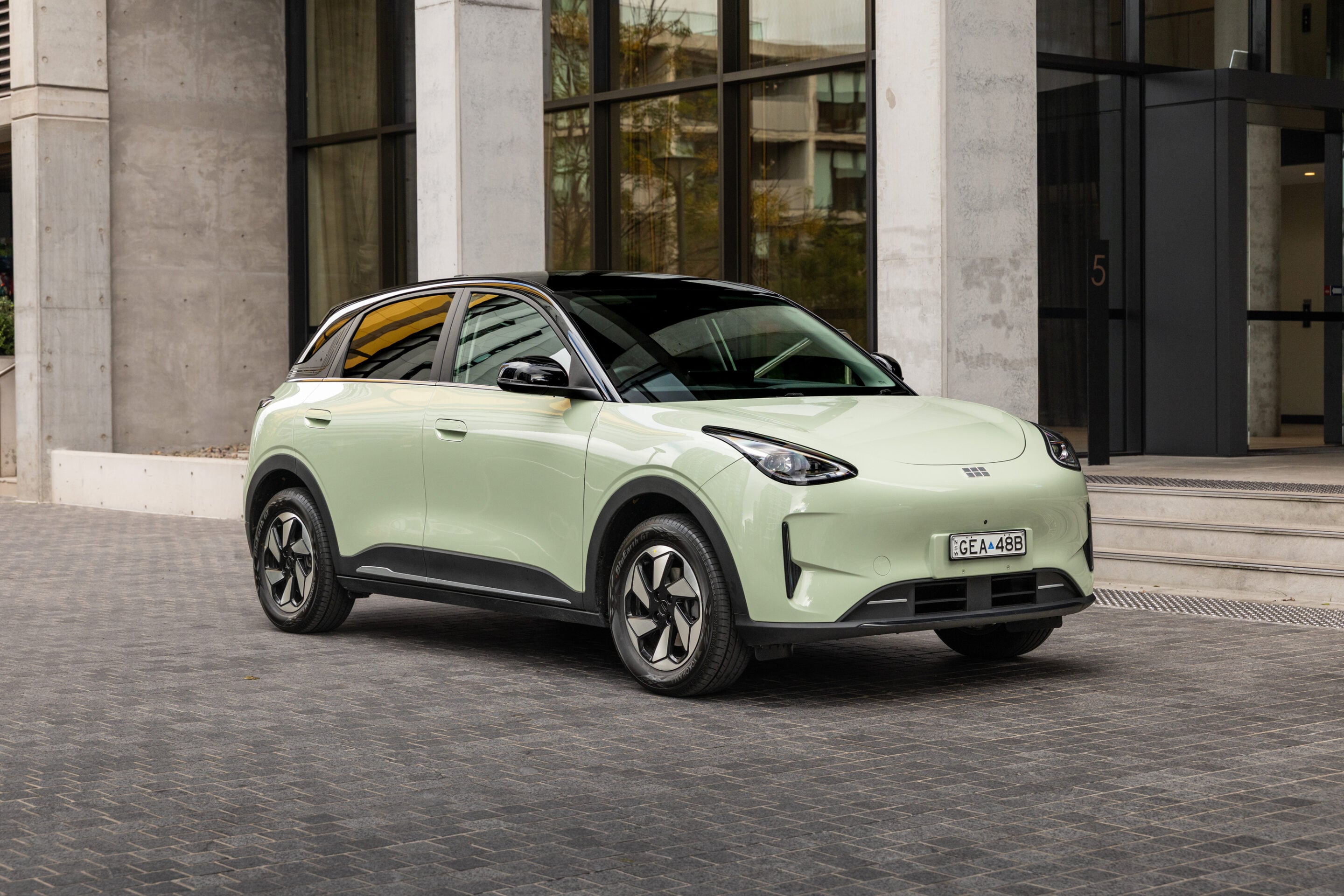Mint-green compact SUV parked on a paved plaza in front of a modern glass-and-concrete building.