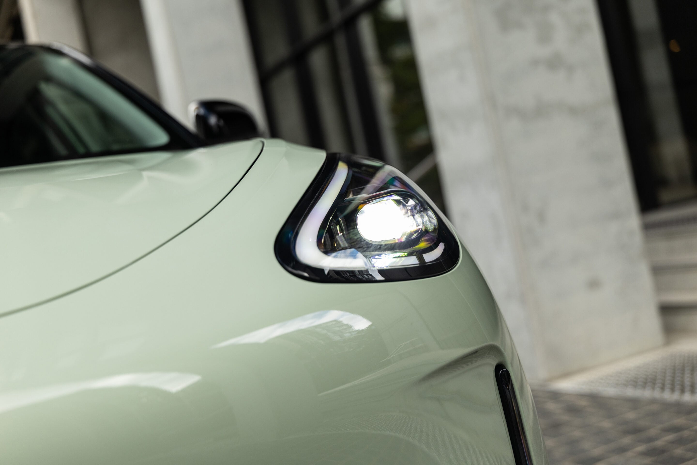 Close-up of a mint-green car's headlight and front fender with a blurred urban background.