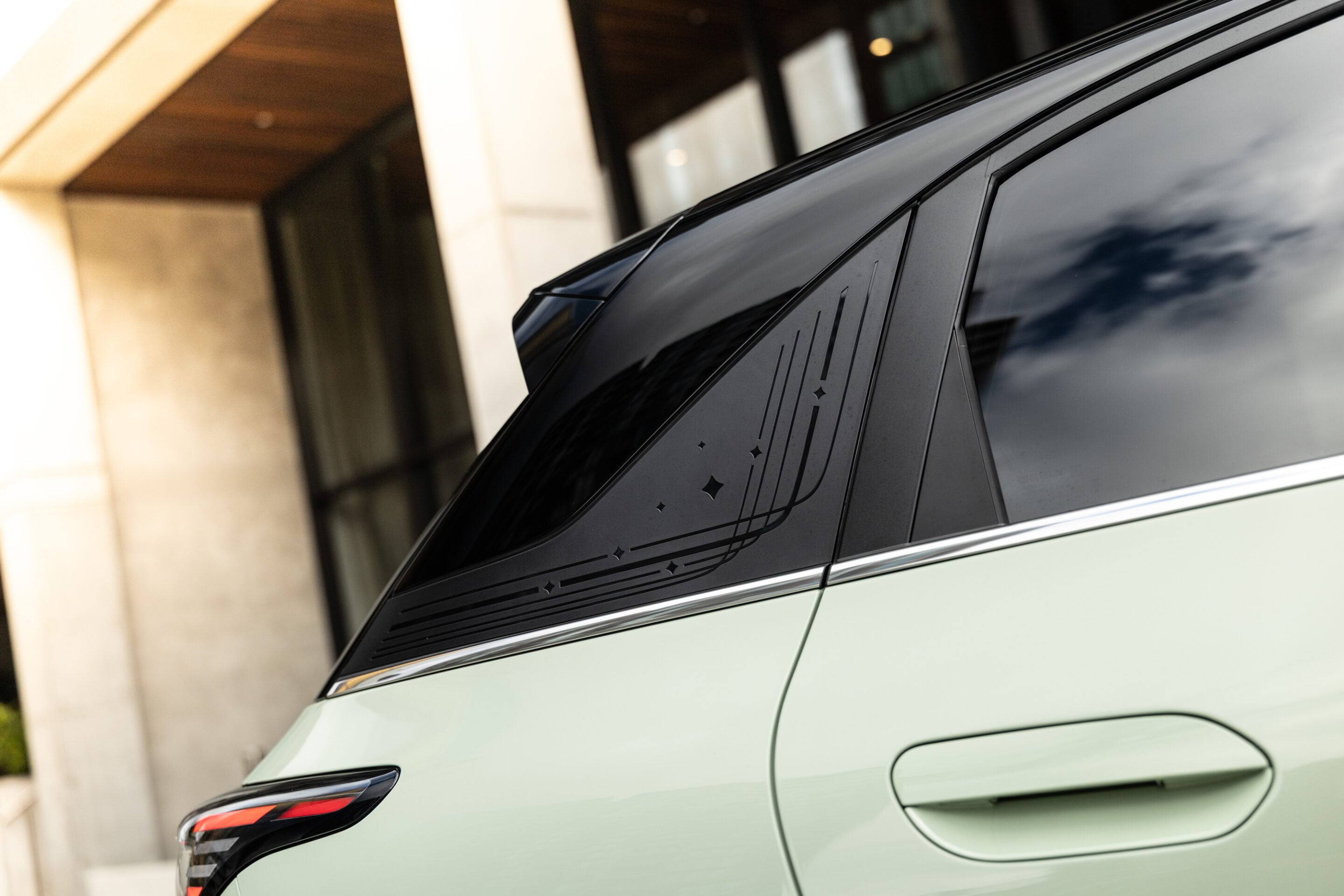 Close-up of a mint-green car's rear side window featuring a black decorative etched pattern and small shapes along the glass.