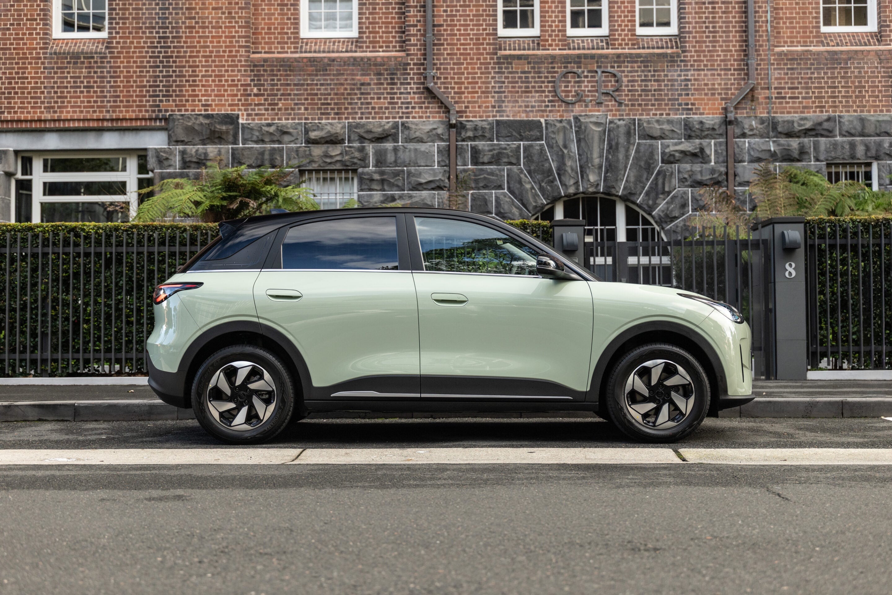Side view of a pale green SUV parked along a curb in front of a brick building with a gated fence and number 8.