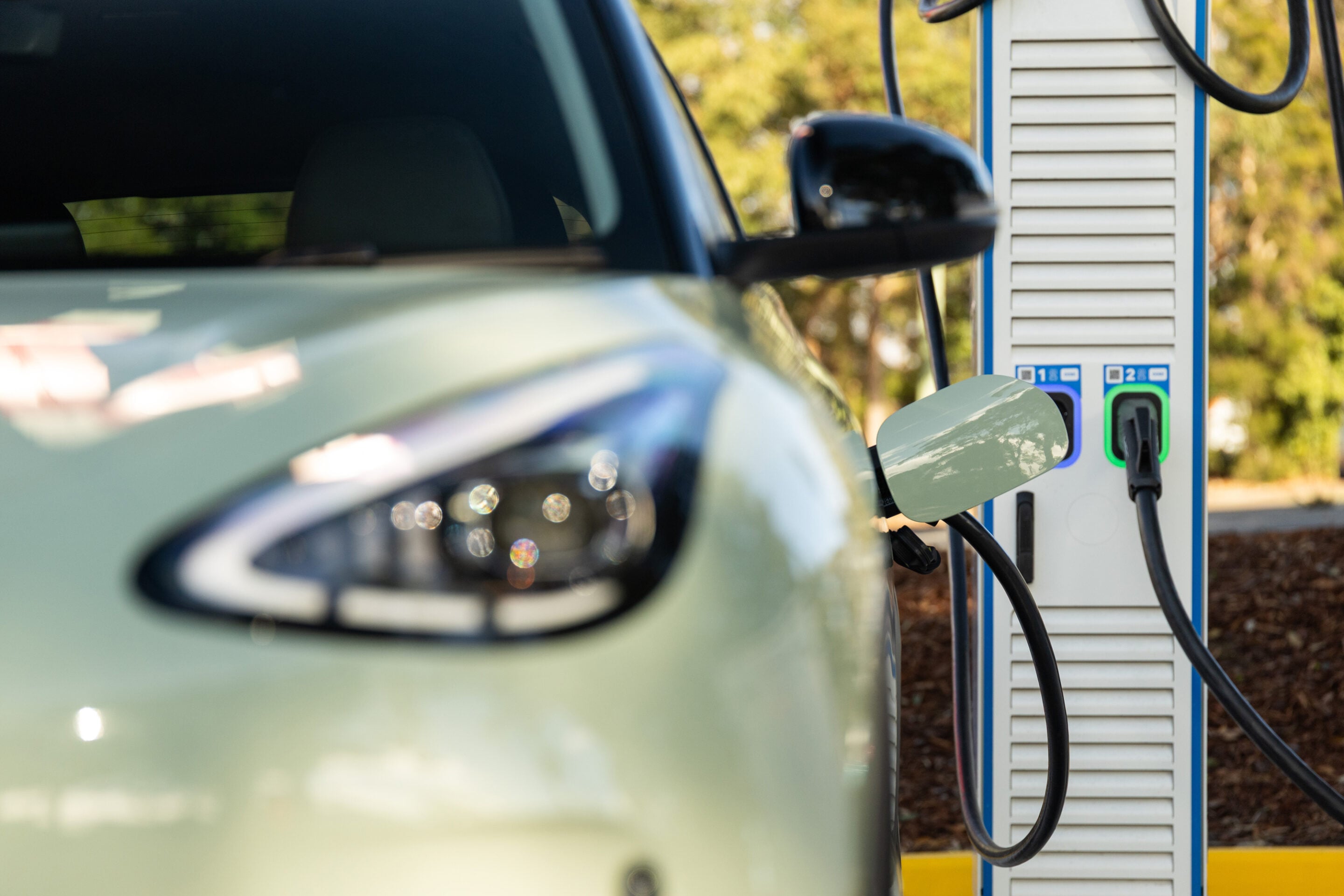 Electric car plugged into a public charging station with a charging cable attached to the vehicle's side port.