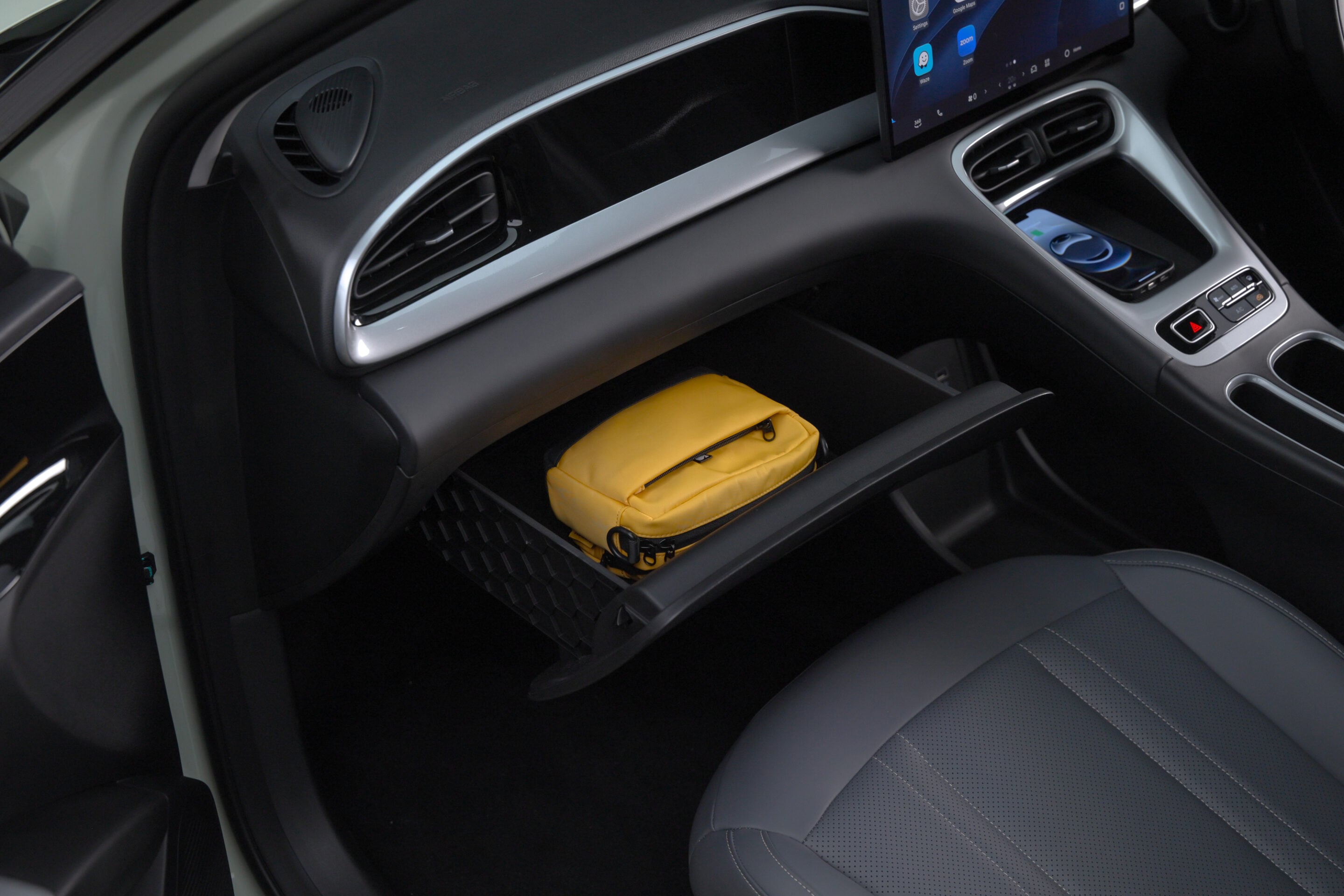 Open glove compartment in a car showing a yellow pouch inside, with the center console and touchscreen visible in the background.