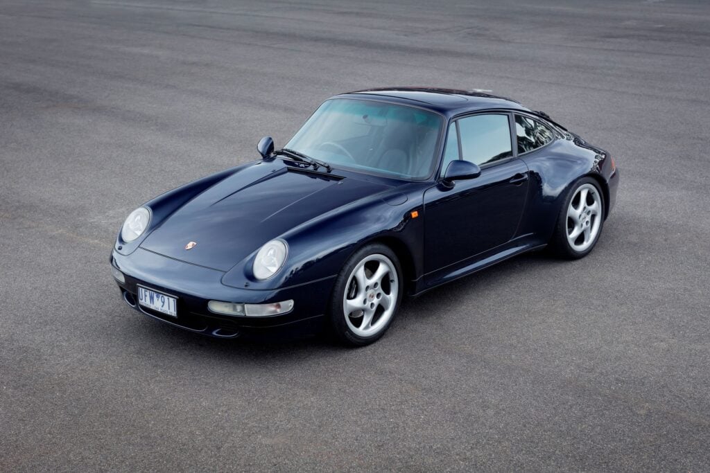 Front-left view of a dark blue Porsche 911 parked on a paved surface, showing rounded headlights and alloy wheels