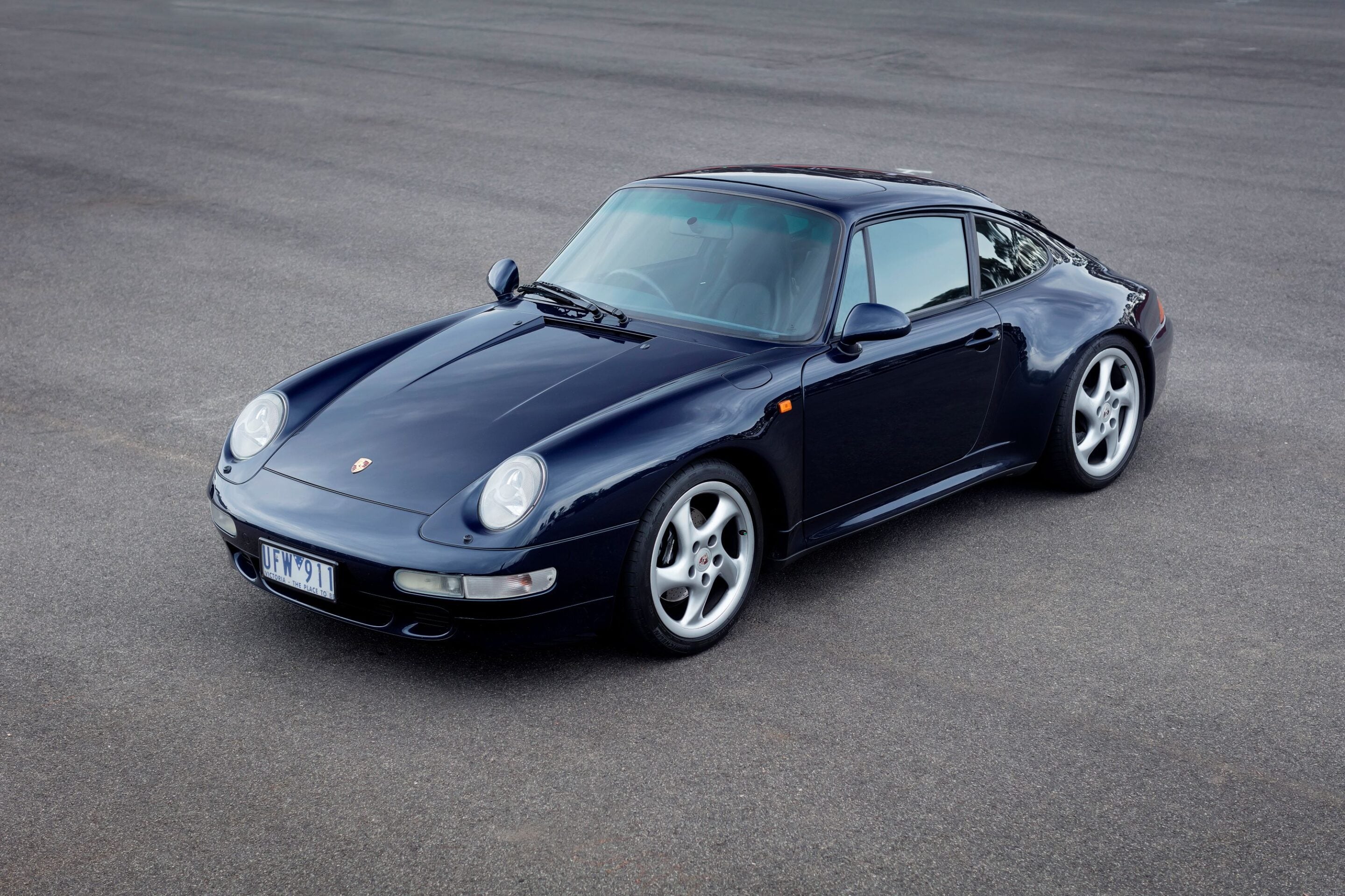 Front-left view of a dark blue Porsche 911 parked on a paved surface, showing rounded headlights and alloy wheels