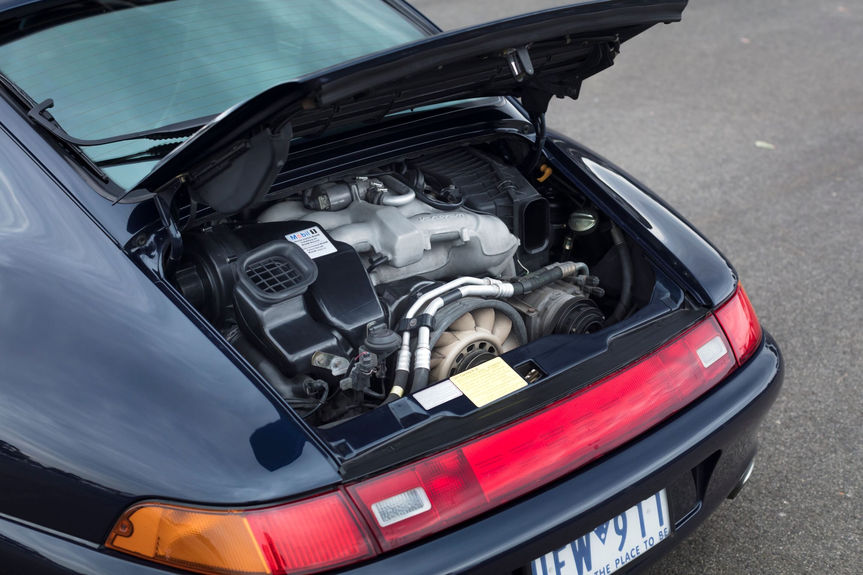 Rear engine bay of a dark blue Porsche with the hood open, exposing the air intake and engine components